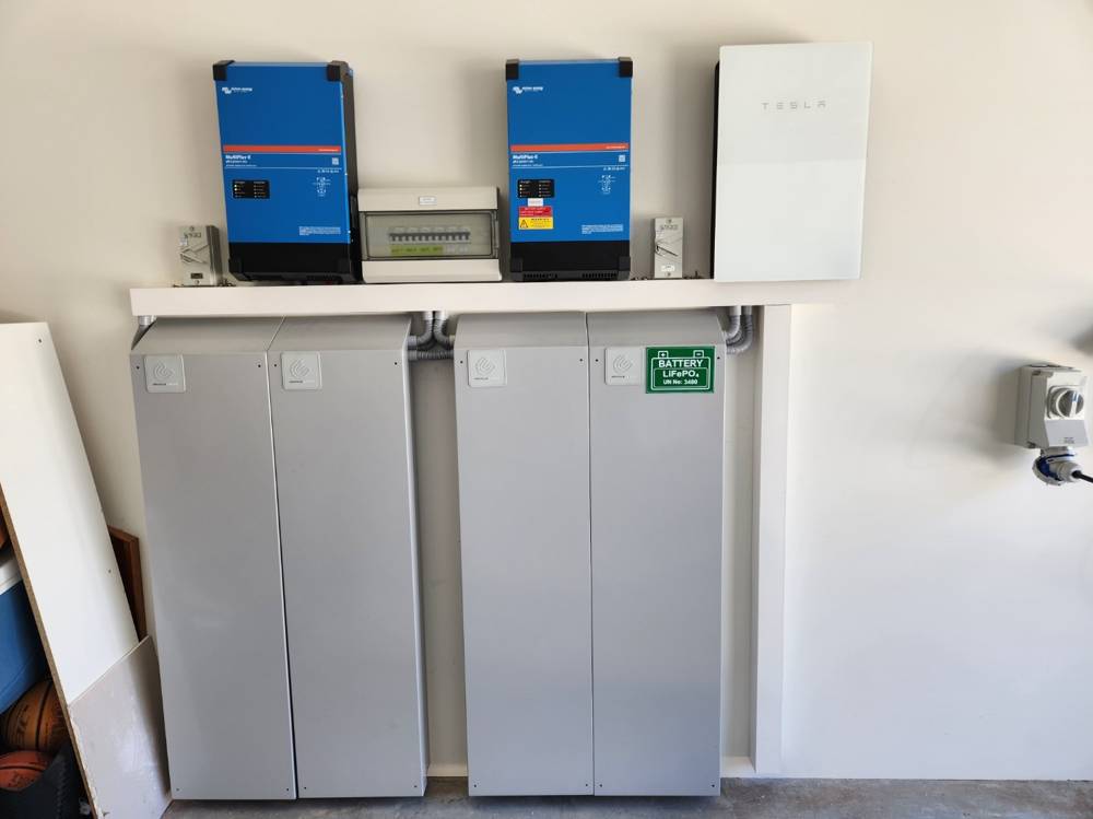 A 40 kWh Upcycle installation of four cabinets under two inverters, with an existing Tesla Powerwall mounted to the right