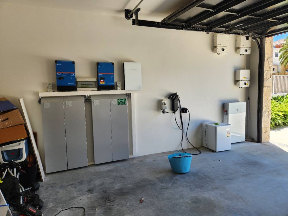 A 40 kWh installation viewed across a garage, with inverters on a shelf above the battery cabinets