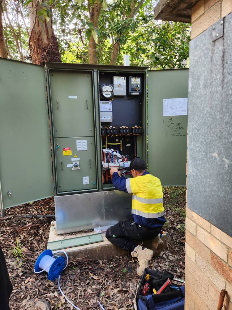 A licensed electrician installing current-transformer clamps inside a site power cabinet